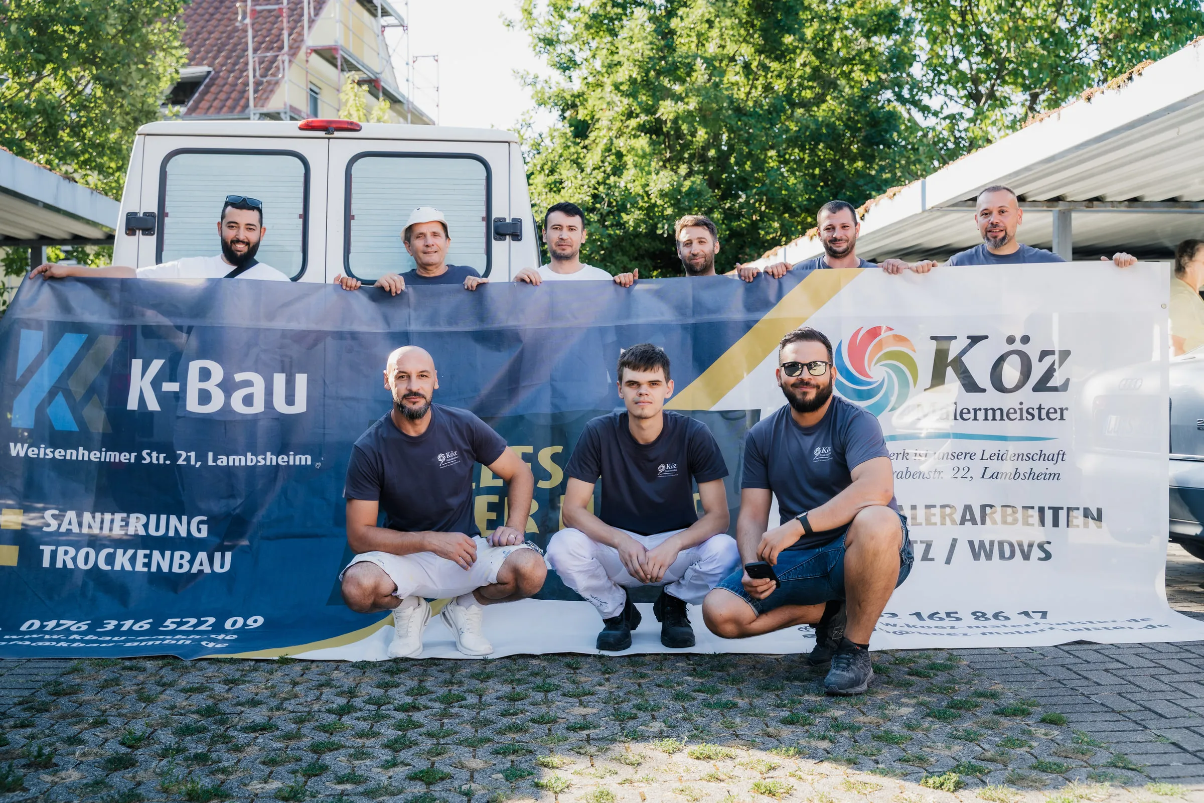 Das Team von KÖZ Malermeister vor dem Firmenfahrzeug mit Firmenbanner.